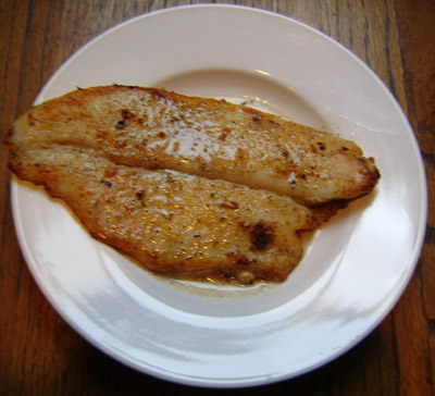 Cooked fish fillet in lemon-butter sauce served on a white plate.