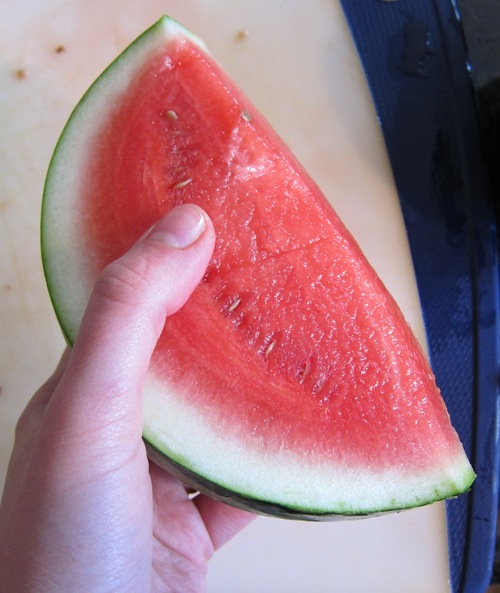 hand holding a slice of red, sweet and juicy watermelon