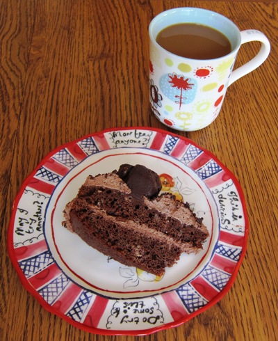 a slice of chocolate truffle cake on a plate and a cup of coffee