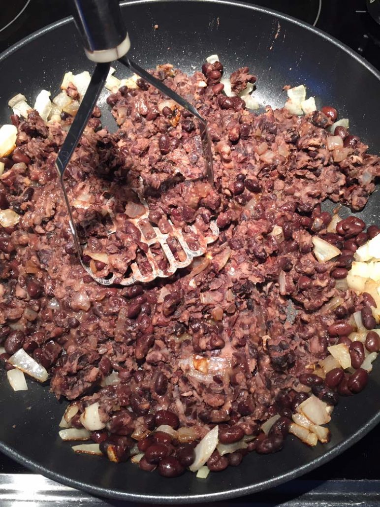 Mashing black beans with potato masher