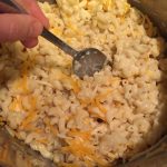 adding shredded cheese to cooked macaroni