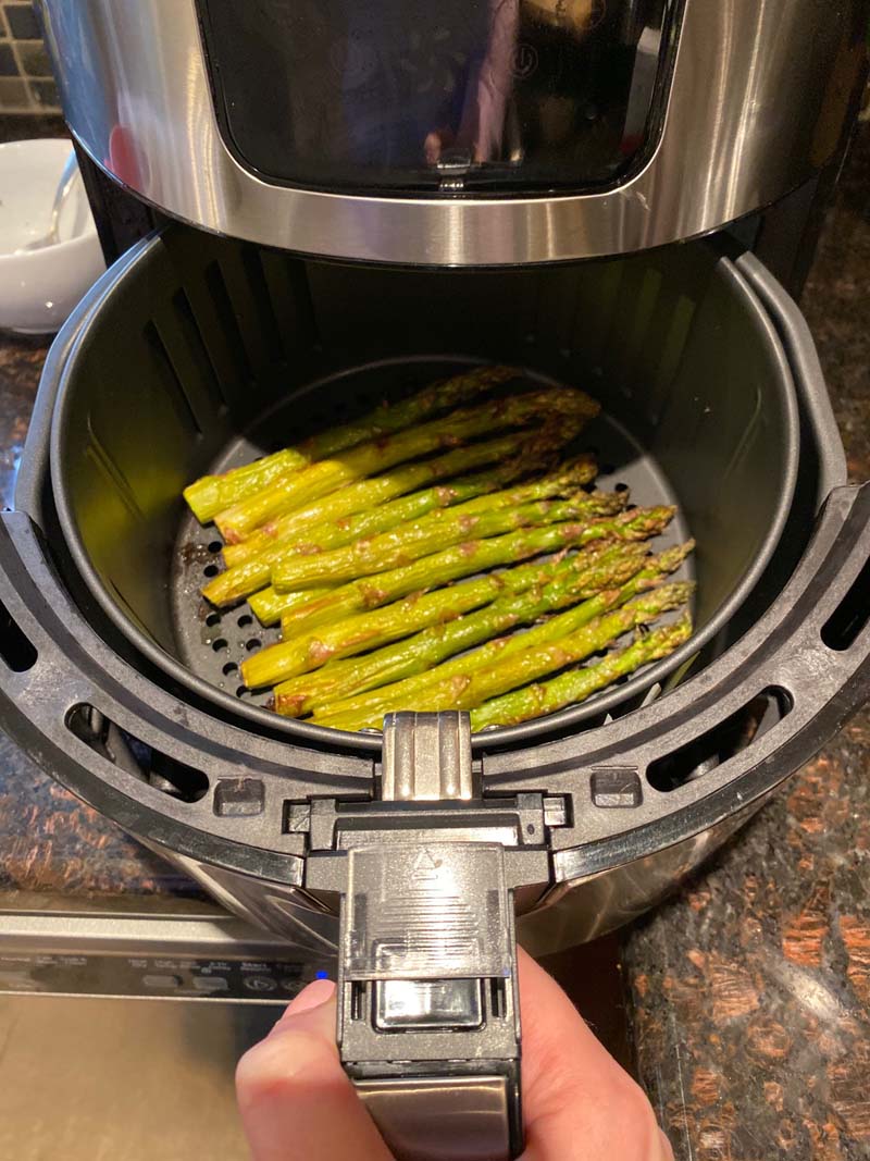 woman pulling roasted asparagus out of the air fryer