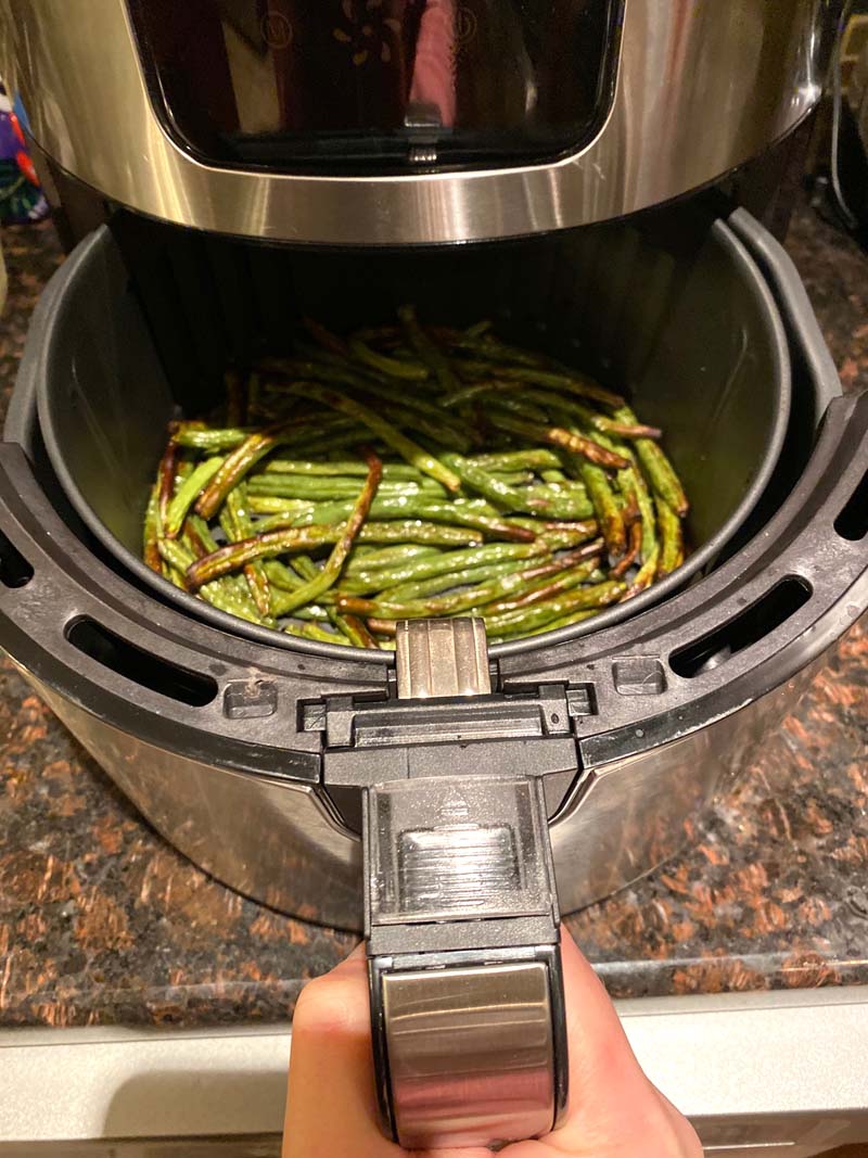 Woman pulling out an air fryer basket filled with green beans.