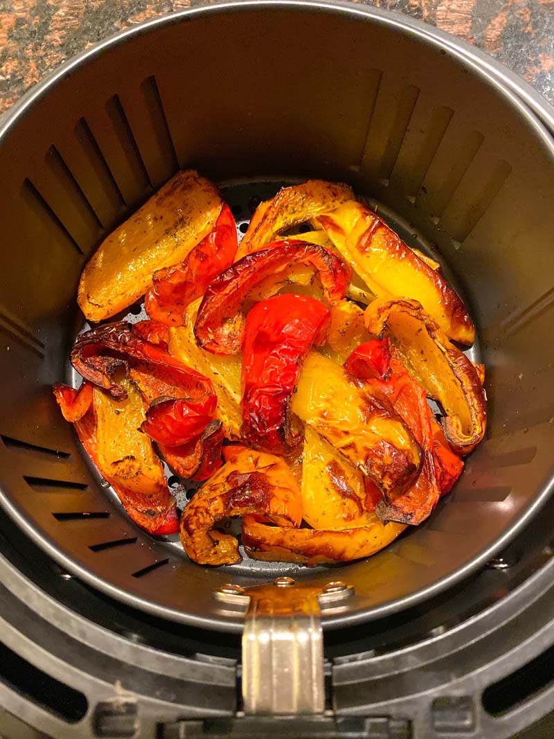 Red, yellow, and orange roasted bell peppers in an air fryer basket.
