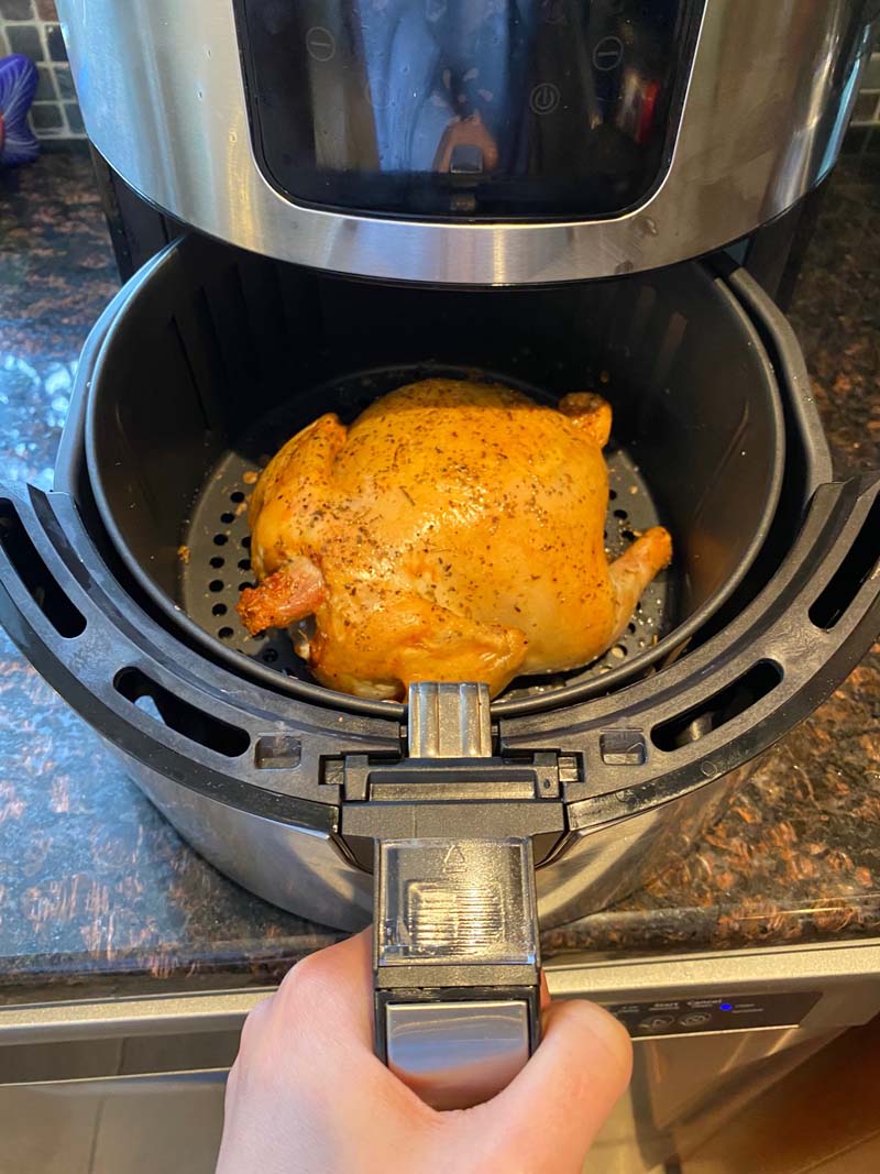 Woman pulling out an aifryer basket with a cornish hen inside