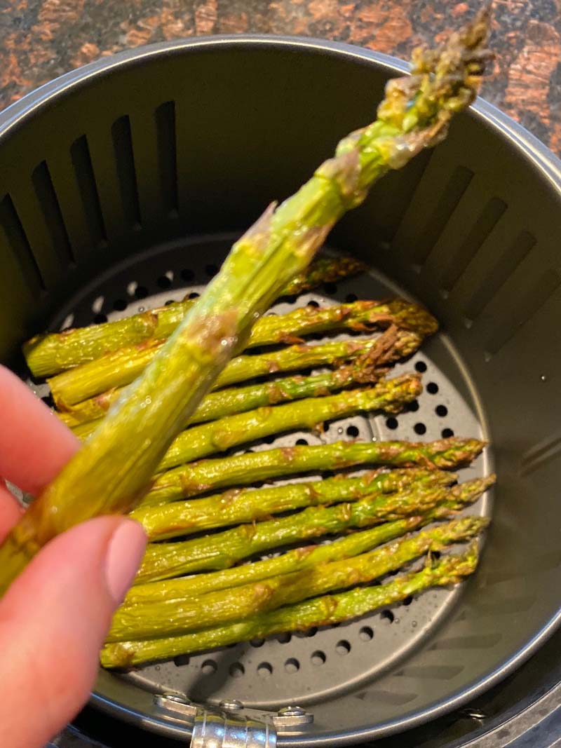 Woman holding up a spear of roasted air fryer asparagus