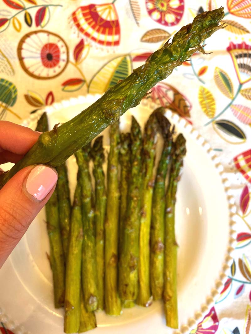 Woman holding an air fryer roasted asparagus stalk.