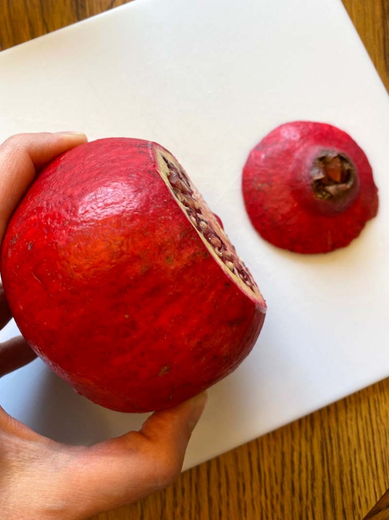 Woman holding a pomegranate with the top cut off over a cutting board.