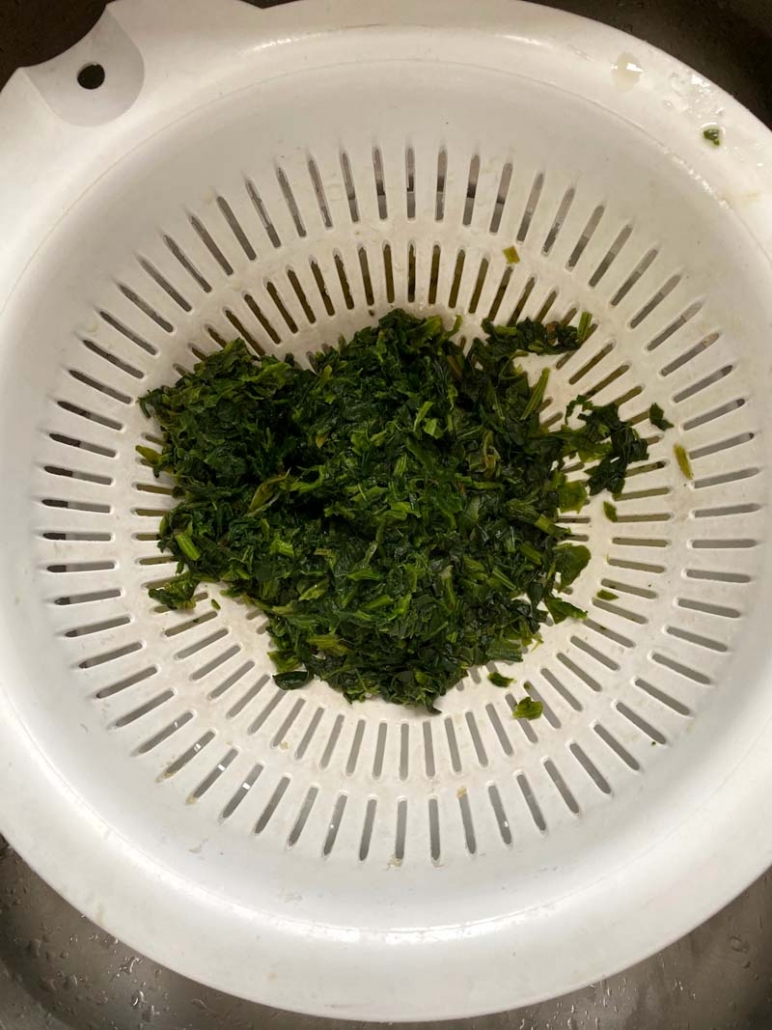 Colander with chopped spinach at the bottom