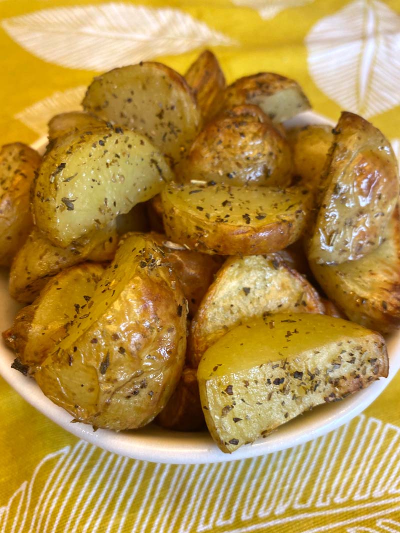 White bowl of roasted potatoes with herbs sprinkled on