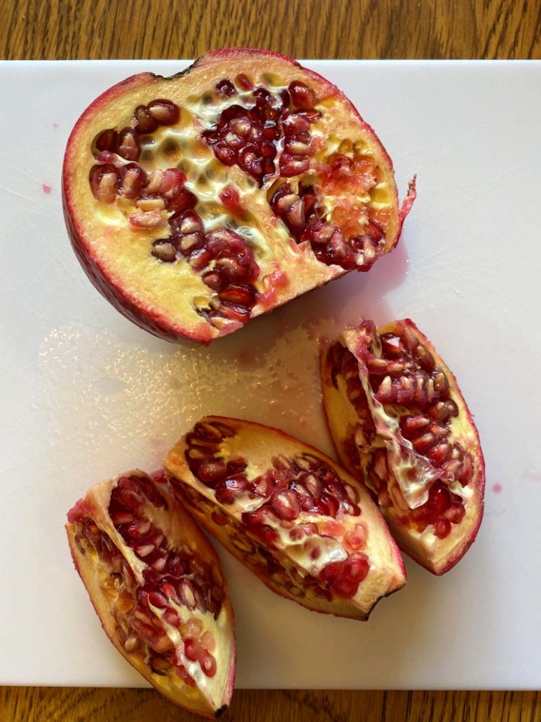 2 halves of a pomegranate. One half is intact while the other is sliced into 3 sections.