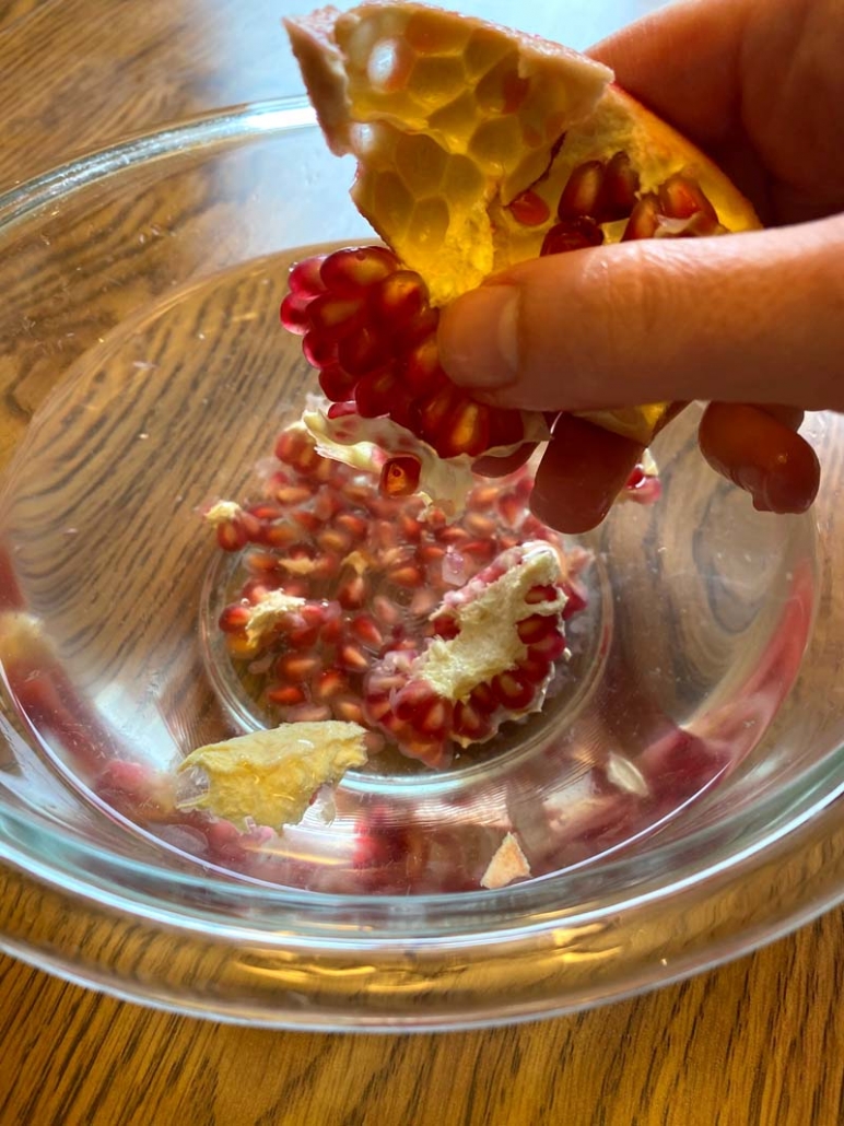 Woman holding a pomegranate section over a bowl of water, pushing the seeds into the water