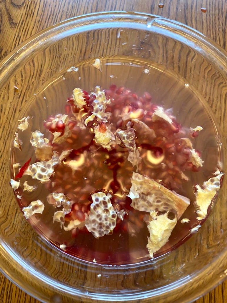pomegranate seeds in a water bowl with pomegranate membranes floating at the top