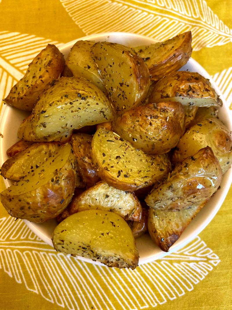 Roasted potatoes with skins in a bowl placed on a yellow tablecloth 