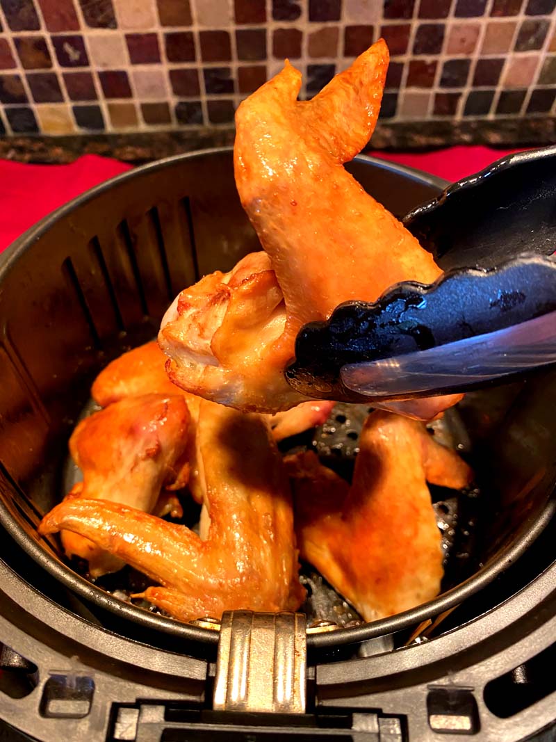 Taking teh wings out of the air fryer with tongs