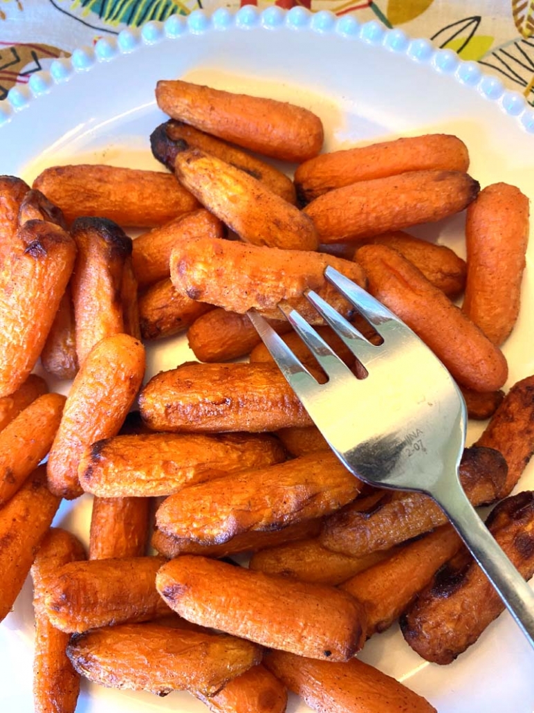 eating roasted baby carrots on a white plate