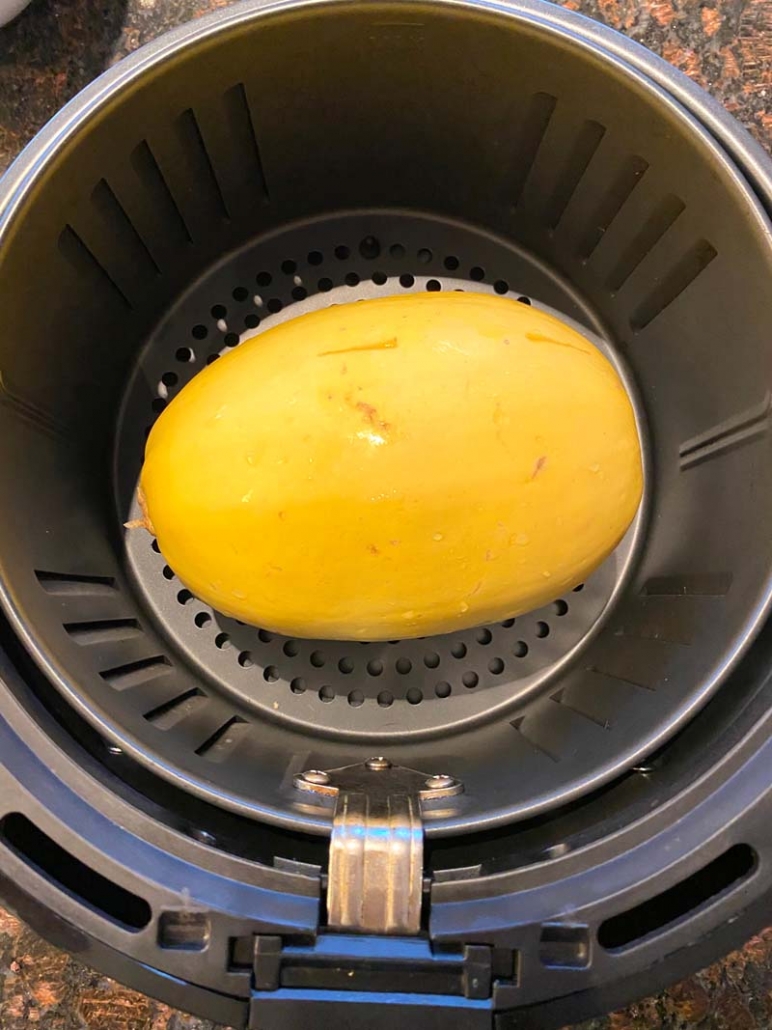 raw whole spaghetti squash in an air fryer basket 