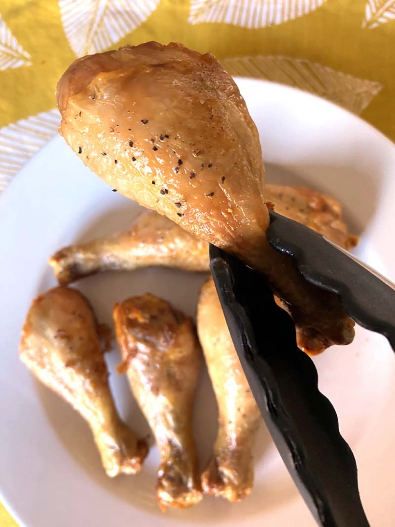 holding a cooked chicken leg with tongs