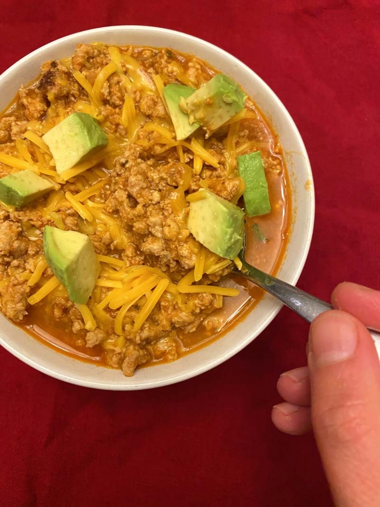 low carb chili topped off with shredded cheese and avocados in a white bowl