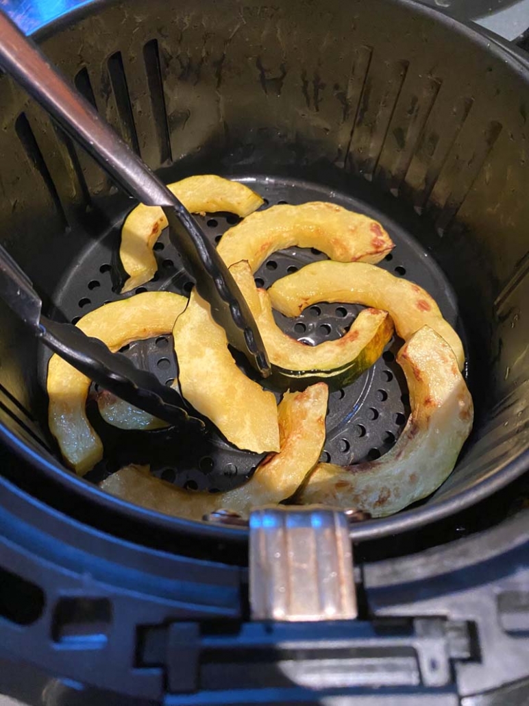 flipping cooked acorn squash fries in air fryer basket