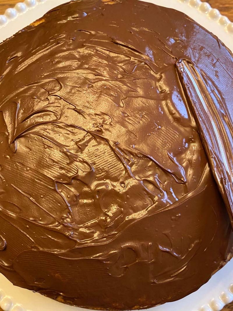 adding chocolate frosting to a vanilla cake with a knife