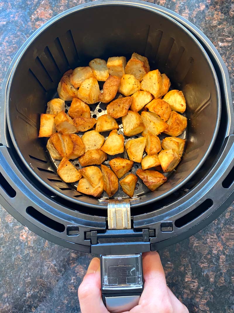 A hand removing the air fryer basket with the potatoes