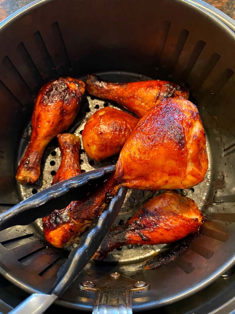 holding barbeque chicken legs with a pair of tongs