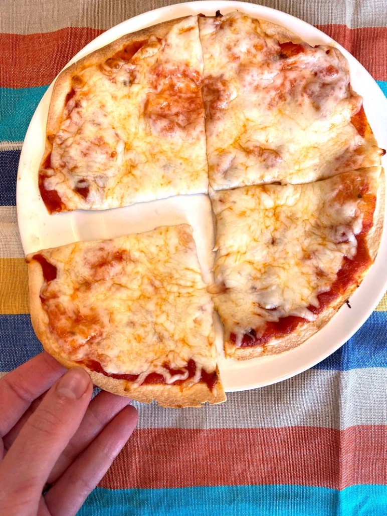 tortilla pizza on a plate with hand taking a slice of pizza