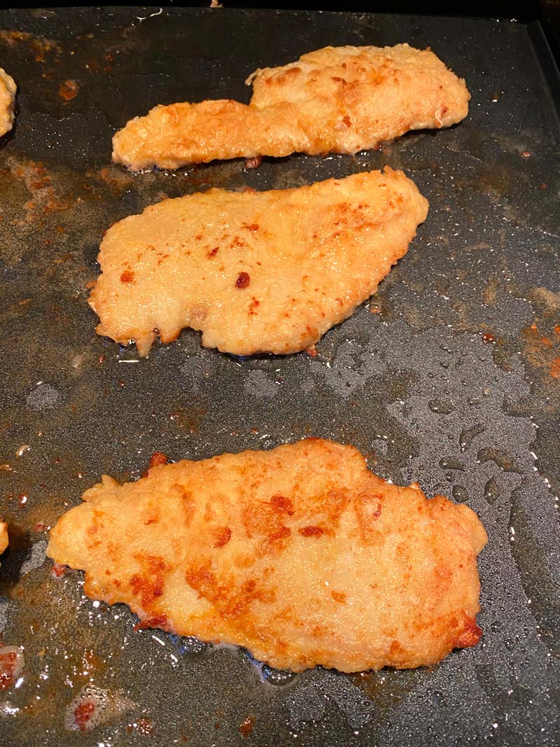 Three pieces of chicken frying on a griddle