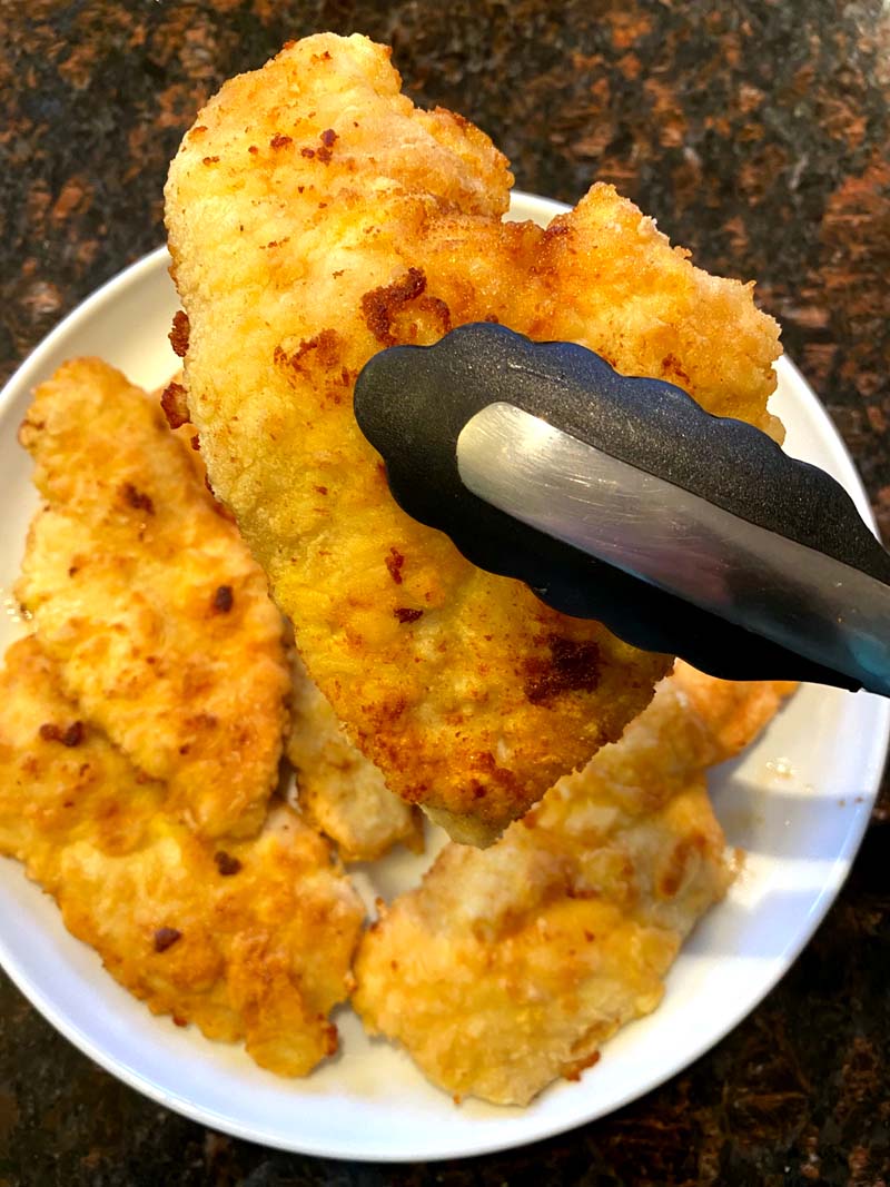 A piece of fried chicken being held with tongs