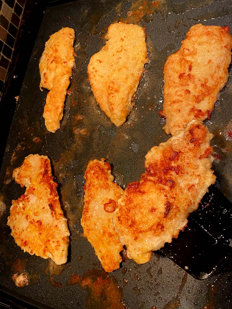 Pieces of chicken frying on a griddle