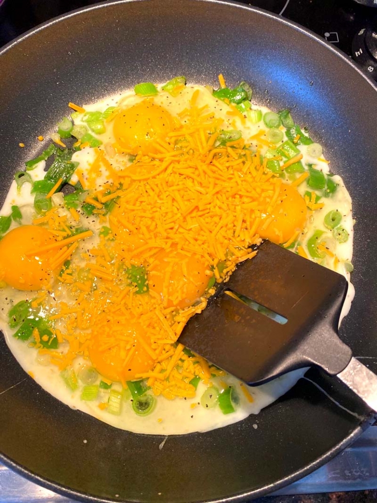 adding eggs, green onions, and shredded cheese to a pan 