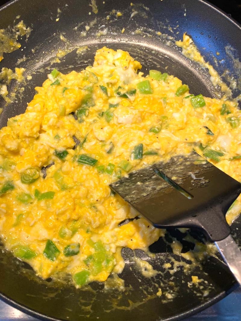 cooking eggs with green vegetables in a saute pan