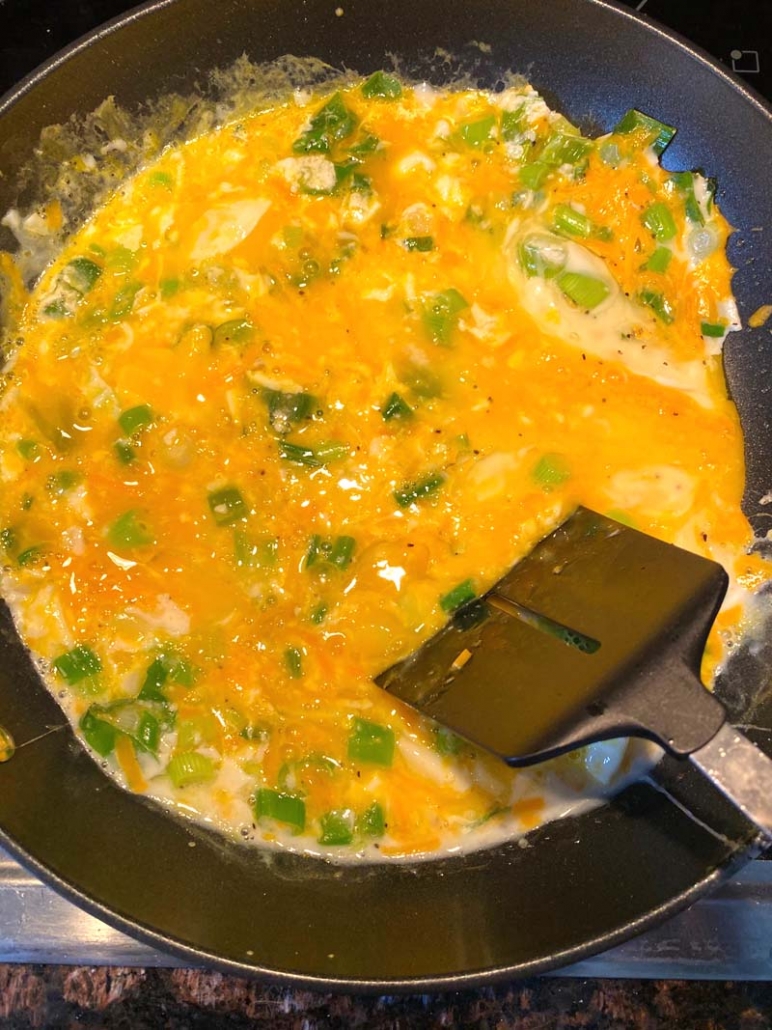 melted cheese on scrambled eggs with green onions