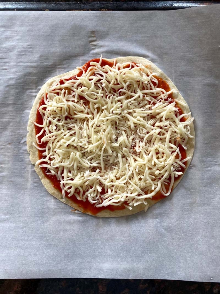 tortilla pizza spread with tomato sauce and sprinkled with shredded cheese