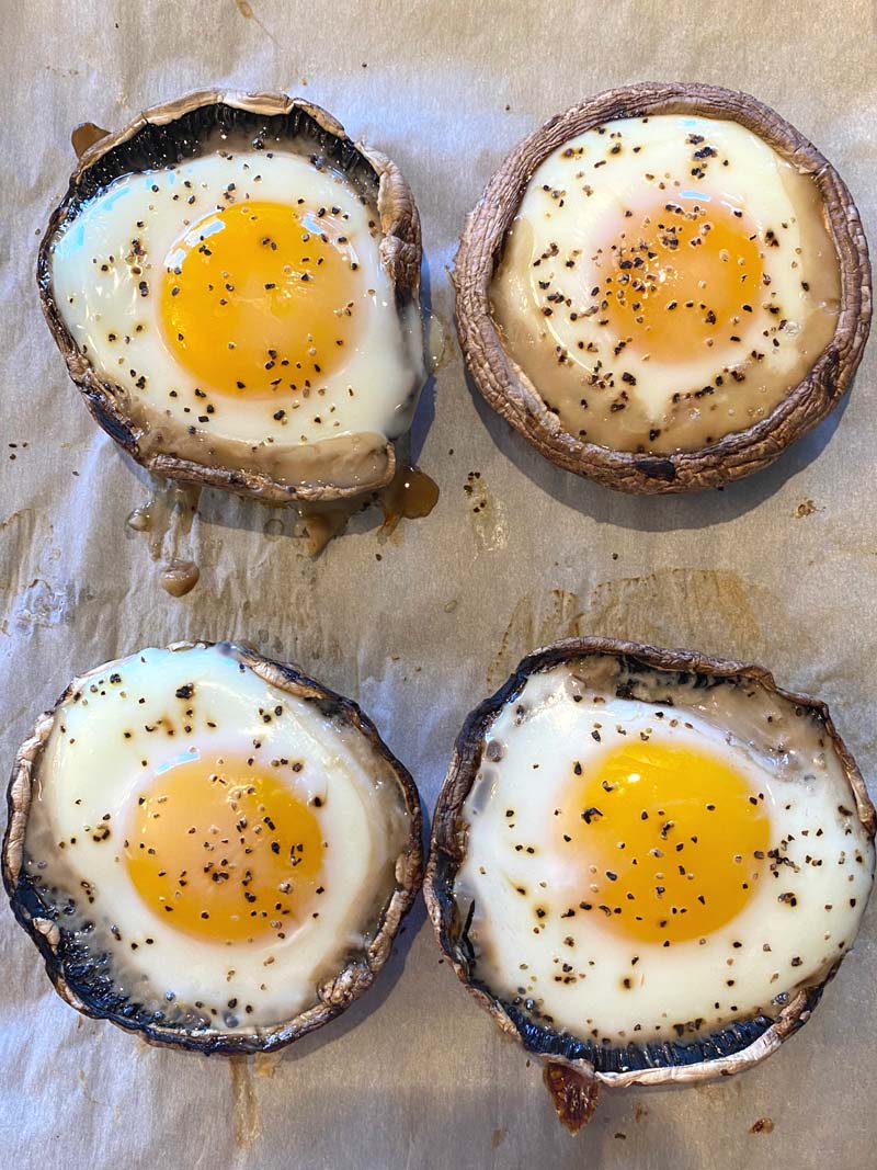 Four baked portobellos with eggs on parchment paper