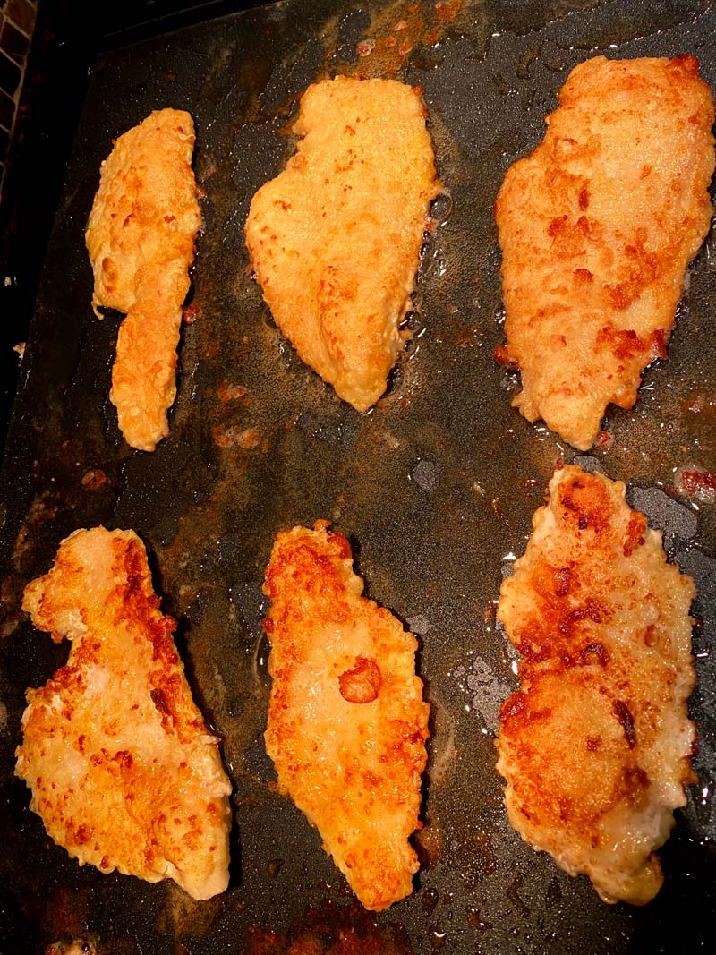 The pan fried chicken being cooked on the griddle