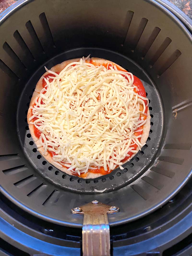 Cheese and tomato sauce on the pizza in the air fryer basket