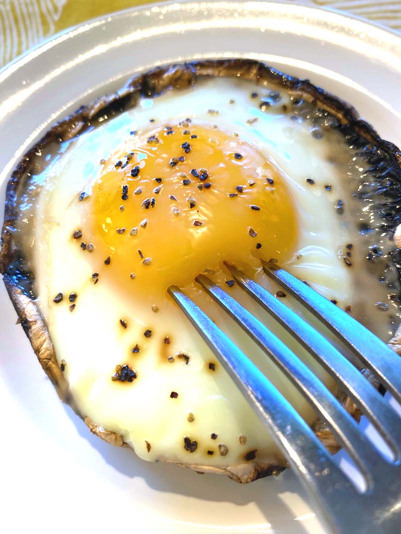 A fork breaking the yolk in the baked egg