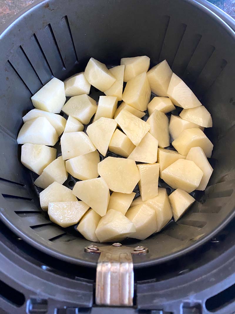 The uncooked potatoes in the air fryer basket