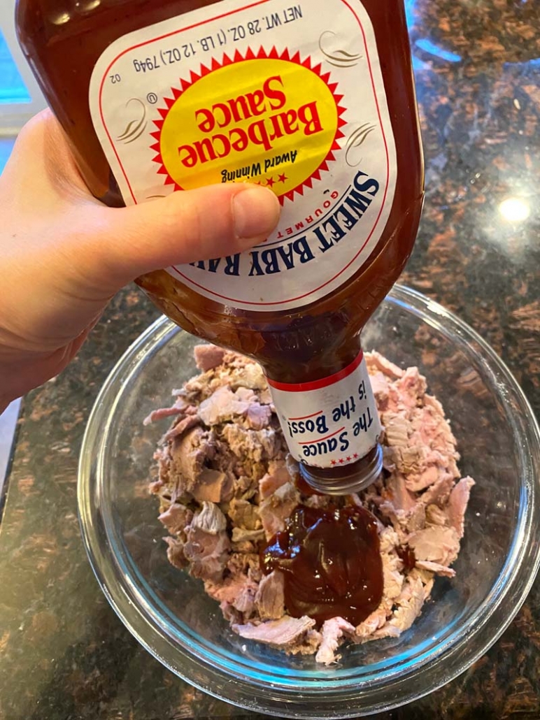 pouring bbq sauce into bowl with shredded beef 