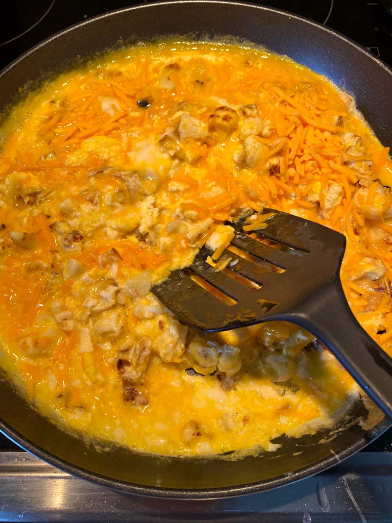 A spatula moving the eggs and cauliflower in the skillet