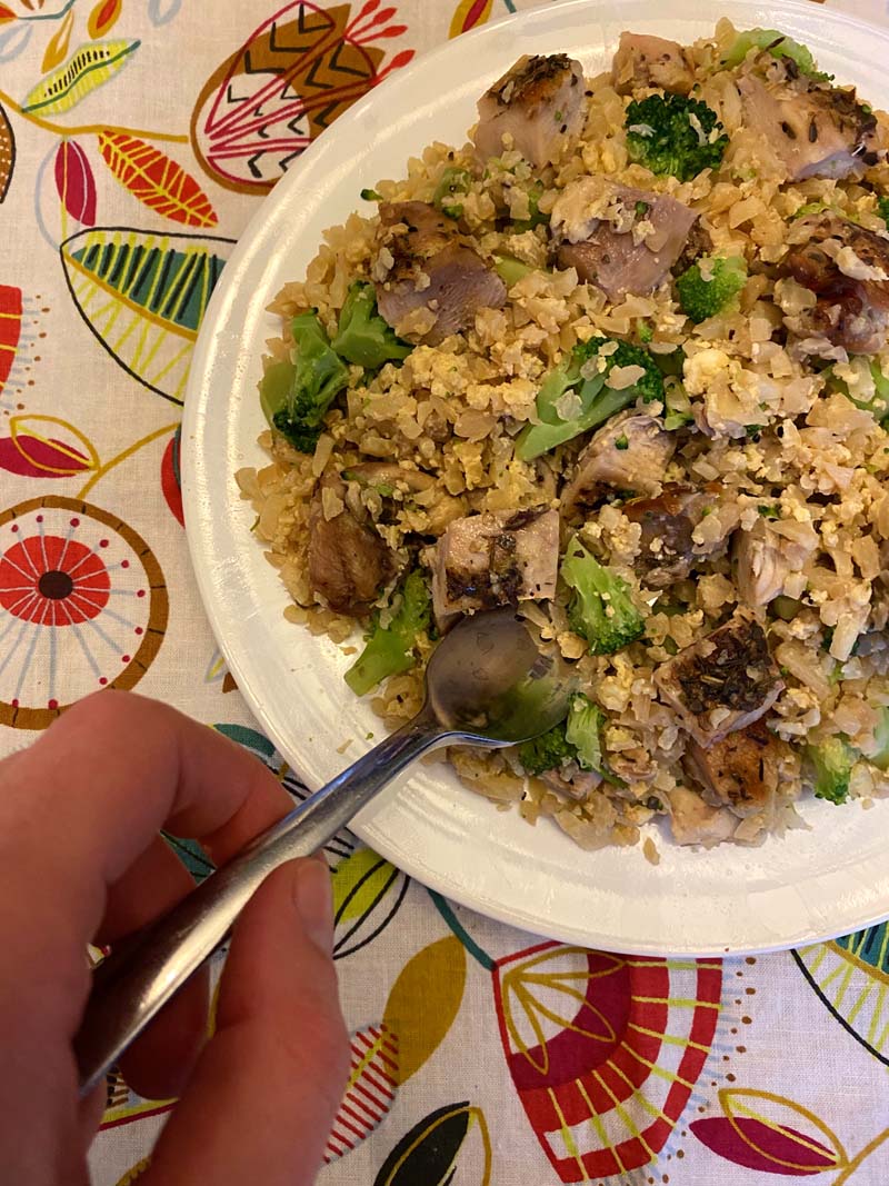 woman taking a spoonful of chicken cauliflower fried rice 