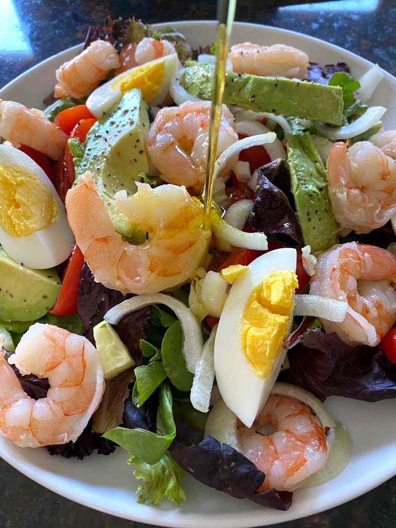 A homemade dressing of olive oil and lime juice being poured on a salad 