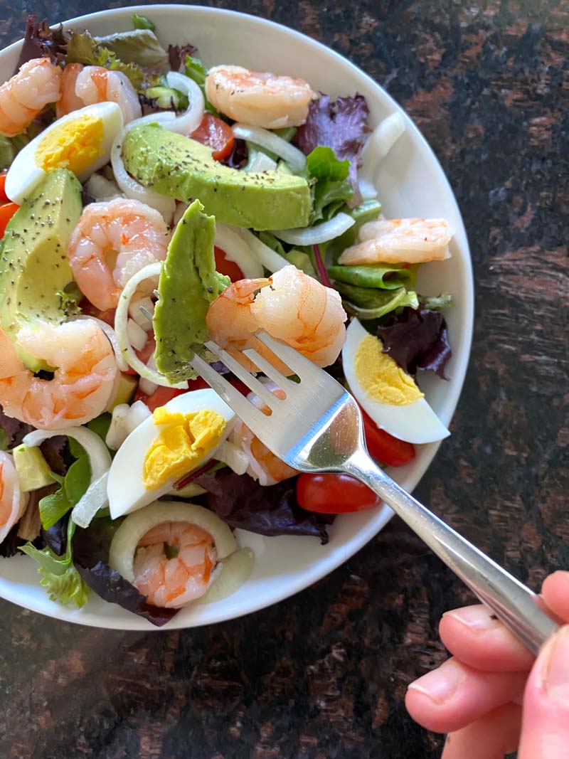 A fork eating shrimp egg avocado salad 