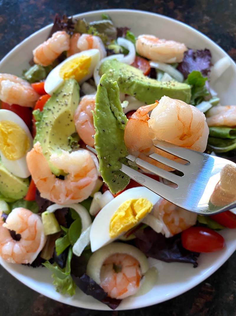 A bowl and fork showing how to eat shrimp egg avocado salad 