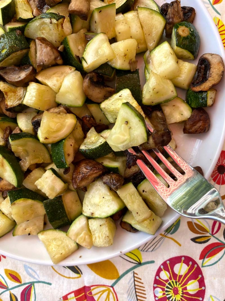 eating zucchini and mushrooms with a fork on a white plate 