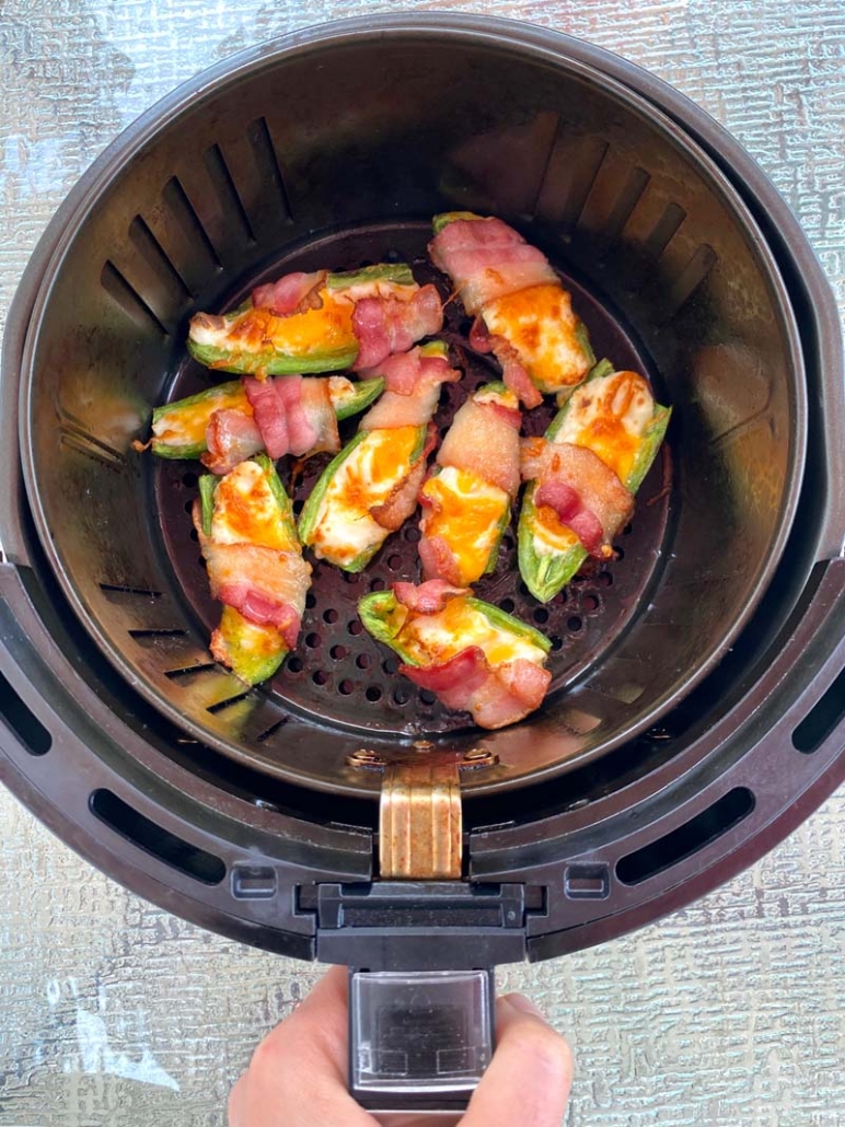 Pulling the air fryer basket out - inside are cooked bacon-wrapped jalapeno poppers
