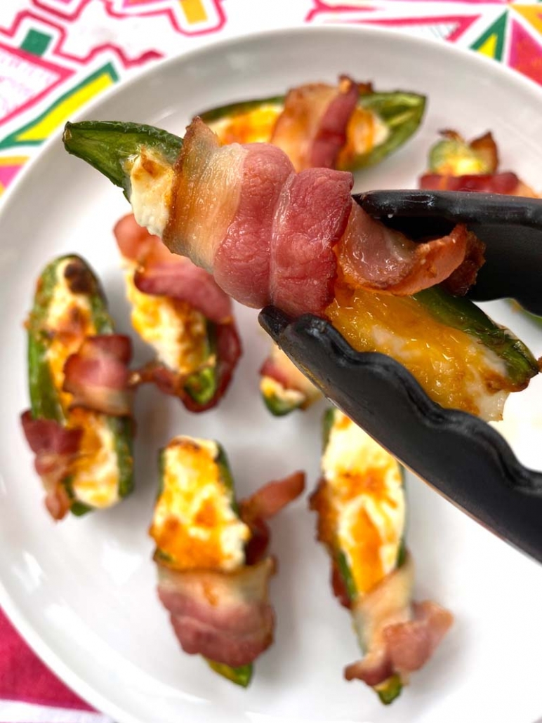 A bacon-wrapped jalapeno popper in a pair of tongs