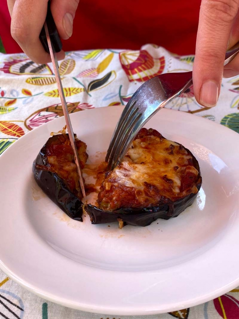cutting to a mini eggplant pizza with a fork and knife